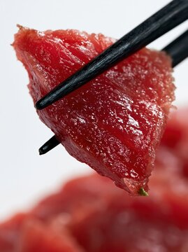 Fresh Bluefin Tuna Maguro Sashimi Cube Held by Black Chopsticks Macro Japanese Sushi Cuisine Photography on Clean White Background