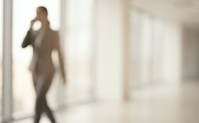 Fototapeta premium A blurred image of a businesswoman in a suit, walking confidently while using a smartphone. The setting is an office with large windows, creating a professional atmosphere.