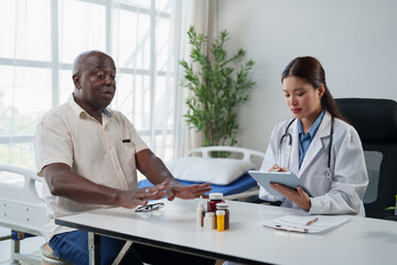 Asian female doctor having a consultation with an African American senior patient about his health, medications, and treatment plan in a hospital examination room © Tj
