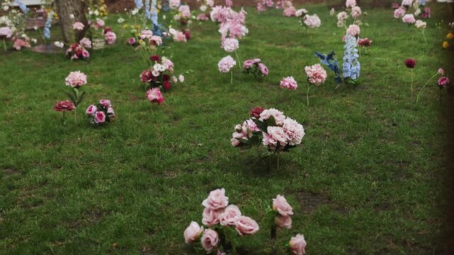 Raining on wedding party decor luxury flowers in green grass lawn close up 4K. Moody outdoor ceremony cinematic scene with pouring rain drops on wet blooming plants in forest meadow in slow motion.