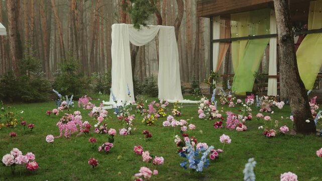 Stormy rain at wedding party decor with close up marriage arch draped in white fabric 4K. Elegant medium shot of outdoor ceremony altar decoration with wet flowers in forest during summer rainy
