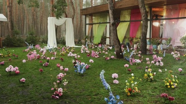 Pouring rain at wedding party decor with luxury lawn flowers and marriage altar in forest 4K. Elegant outdoor ceremony installation on green grass meadow near wooden terrace during summer rainy