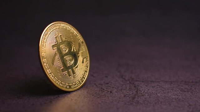 Golden bitcoin cryptocurrency coin standing vertically on a dark granite surface in a studio environment while the camera performs a slow push in movement