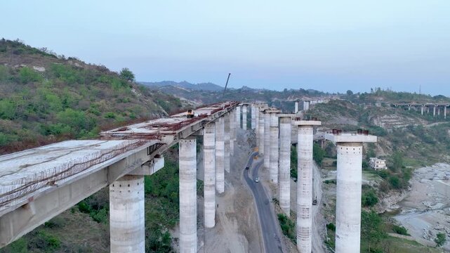 Active civil engineering: Crane lifting materials onto bridge pillars.Cinematic aerial drone establishing shot of a massive highway flyover