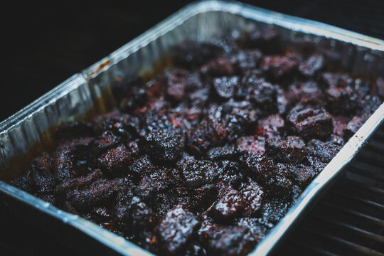 Pork Belly Burnt Ends cooked until black on a pellet grill smoker. The delicious morsels of fatty pig meat are resting in a tinfoil pan ready to eat for dinner. 