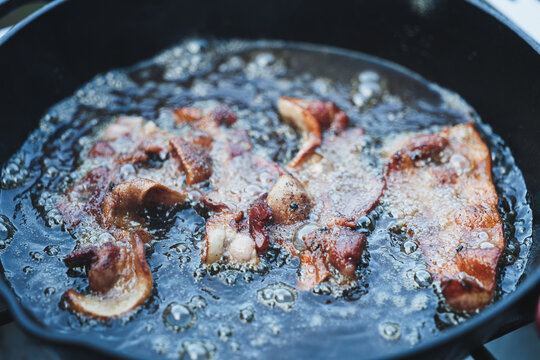 Fresh bacon sizzling in grease and oil on a cast iron skillet. The pan is hot and the pork is delicious. Great for breakfast, lunch, and dinner the tasty treat is loaded with fat, generally unhealthy.