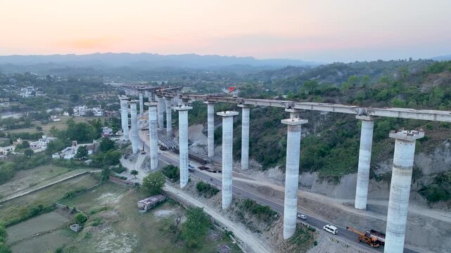 Aerial shot of Massive highway bridge construction showing giant concrete pillars for new flyover. Cinematic aerial drone establishing shot of a massive highway flyover