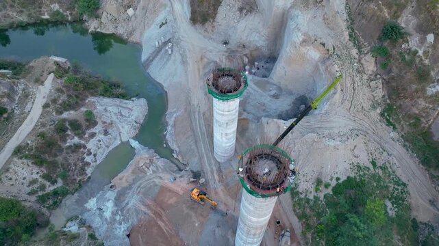 Massive concrete pillars of incomplete highway flyover in India. Sweeping aerial drone shot showcasing the stark contrast between towering, modern concrete bridge pillars