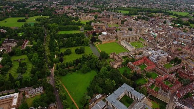 4K aerial view centred on King's College Chapel and front court lawn with the River Cam, The Backs and Cambridge town extending into the distance under summer sky.