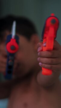 Young boy aiming colorful toy blasters toward camera during playful indoor game expressing imagination childhood excitement and carefree pretend action at home
