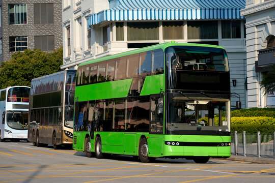 A row of double-decker buses of different colors on the side of a city street. The first one is green.