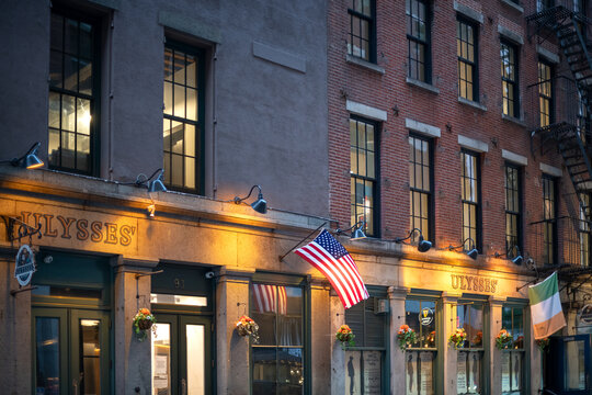 An Irish pub named Ulysses sits on the ground floor of a classic apartment building in downtown Manhattan New York featuring the flags of the United States and Ireland.