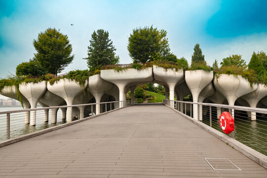 People walk along the bridge leading to Little Island at Pier 55 in Chelsea, an innovative public park featuring unique concrete tulip structures and lush green landscapes in New York City.