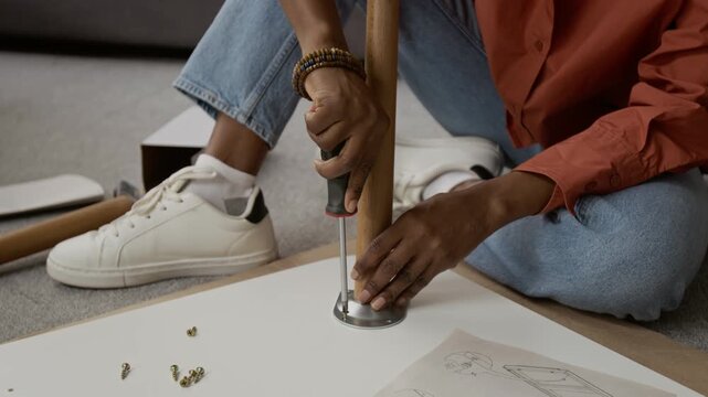 Midsection shot of unrecognisable girl wearing orange shirt, blue jeans and white sneakers using screwdriver to attach wooden leg to white table top