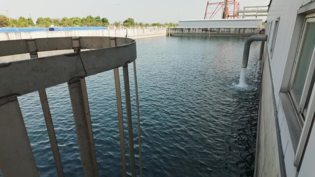 Water flowing from an industrial discharge pipe into a large storage basin, creating gentle ripples on the surface.