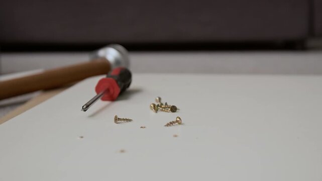 Extreme close-up shot of screwdriver and several small brass screws scattered on smooth white wooden surface