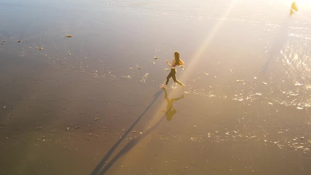 Aerial shot of a fit asian woman jogging on the beach at sunset in Southern California. Slow Motion.
