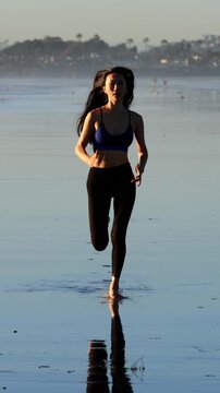 Athletic Asian woman jogging on the beach at sunset in Southern California. Slow motion. Vertical Video.