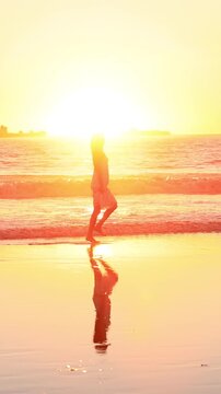 Attractive Asian woman enjoys a walk on the beach at sunset in Southern California. Slow Motion. Vertical Video.