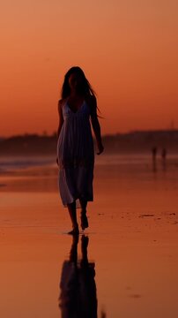 Attractive Asian woman enjoys a walk on the beach at sunset in Southern California. Vertical Video.
