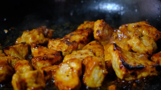 Succulent chunks of meat are frying in a sizzling pan, their edges turning golden brown. A blend of aromatic spices, turmeric and coriander, curry powder, coating every piece in a colorful layer. 