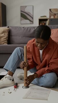 Vertical view of African American girl studying table assembly instructions and securing its leg in place using screws and screwdriver