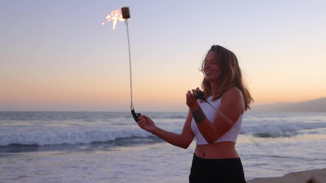 Attractive woman fire dancer spinning flames at the beach. Slow Motion.