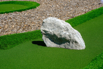 Large rock on a green golf field next to gravel