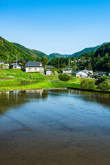 Obraz premium 初夏の美ヶ原高原麓の山村風景と水田への映り込み