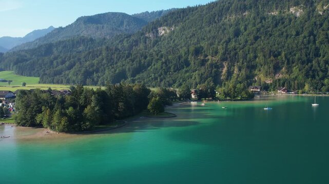 Experience breathtaking aerial views of Wolfgangsee Salzkammergut and its lush surroundings, showcasing serene waters and majestic mountains under a clear sky.
