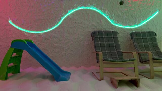 Salt floor wooden chairs halotherapy cave soft pastel lighting casts pink green hues, blue childs slide tucked to side, coarse