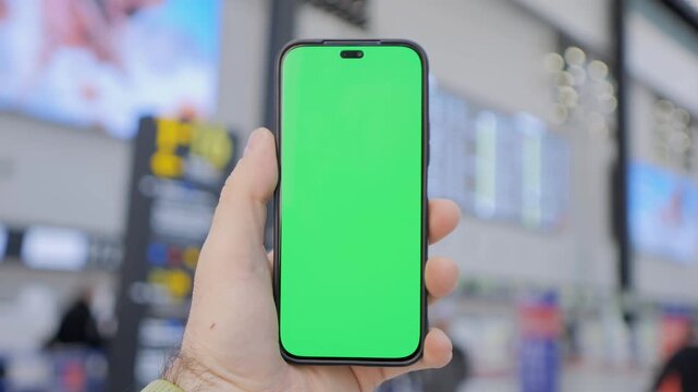 Hand holds phone with green screen. Background shows blurred indoor space. Multiple frames show same scene. No animals or plants shown. Focus on phone and hand only