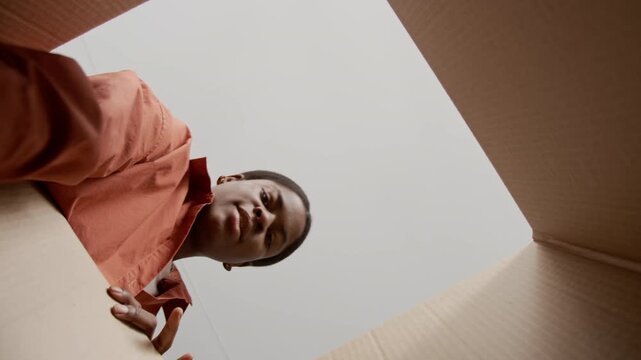 Low angle view from cardboard box of African American young woman packing unwanted clothes