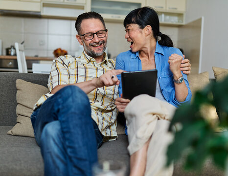 Portrait of a lovely young couple using a tablet computer together and having fun sitting on sofa at home