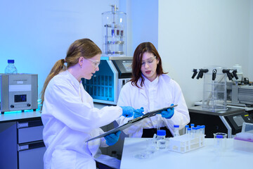 Two Female Scientists Reviewing Data on Clipboard in Modern Research Laboratory