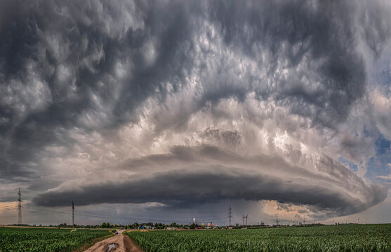 Massive supercell storm cloud above countryside road and green fields
Panoramic view of dramatic rotating supercell thunderstorm over rural landscape with dark cloud formations and severe weather.