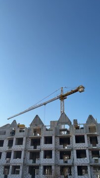 Aerated concrete apartment construction under blue sky, tower crane lifting blocks, exposed blockwork facade with triangular