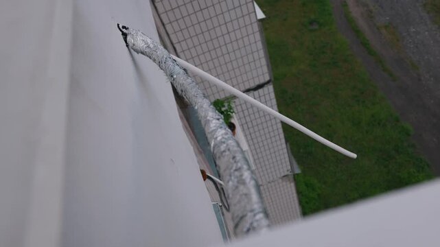 Insulated air conditioning pipes and drainage tubes extend from a tiled building facade above a residential area. Concept of HVAC installation, urban climate control, and residential maintenance