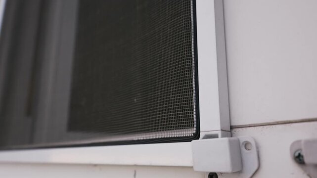 Close-up of a mosquito net installed on a white window frame, focusing on the mesh and corner bracket. Concept of home improvement, summer ventilation, and indoor insect protection.