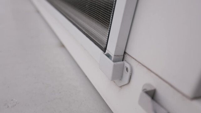 A detailed close-up shot shows a snapped white plastic clip used for securing an insect screen onto a residential window frame. Concept of home maintenance, repair, and property damage.