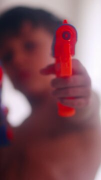 Young boy aiming colorful toy blasters toward camera during energetic indoor playtime expressing childhood fantasy pretend adventure and carefree home entertainment fun