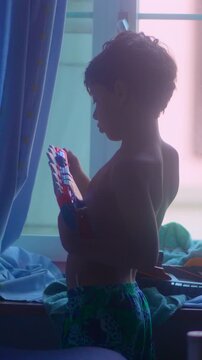 Young boy loading toy blaster near bedroom window during imaginative indoor playtime expressing creativity childhood adventure and authentic everyday home entertainment