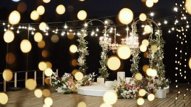 Decorated photo zone on terrace with warm lighting from bulbs and garlands at night. Aesthetic and elegant background decoration of area for evening festive event with many lights.