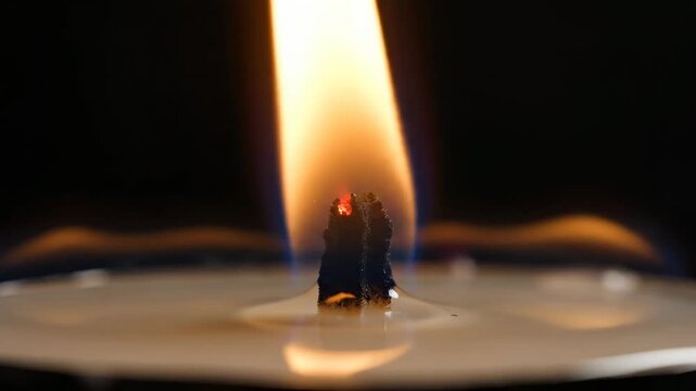 A warm, flickering candle flame ignites the darkness with a radiant orange glow, casting ethereal light on the melting wax and creating a comforting ambiance suitable for reflection