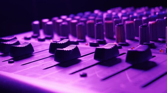 Professional audio mixing console faders are captured from a low angle close up with shallow depth of field in a blue studio. Concept of sound engineering, music production, and audio.