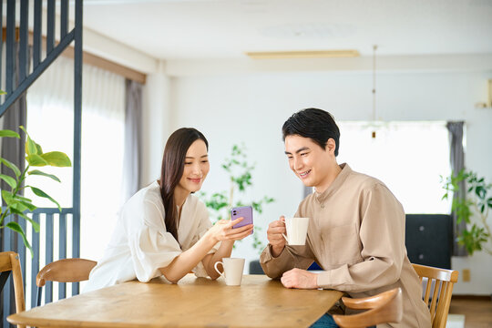 スマホを見ながらコーヒーを飲む夫婦　リビングで会話する恋人
