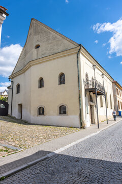 The Jewish synagogue in Boskovice, Czechia stands as a historical structure. The building features distinctive windows and a unique entrance. People walk nearby on the street.