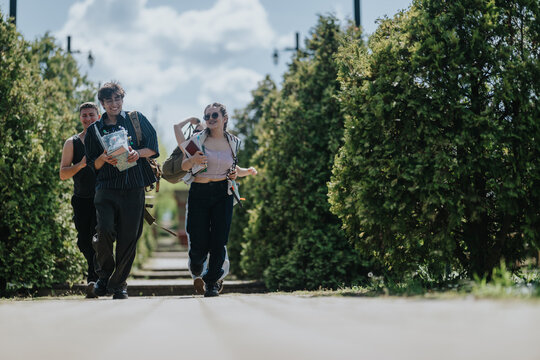 Three young friends walk together along a tree-lined path carrying books and backpacks. A cheerful student group strolls outdoors on a sunny day between green hedges.