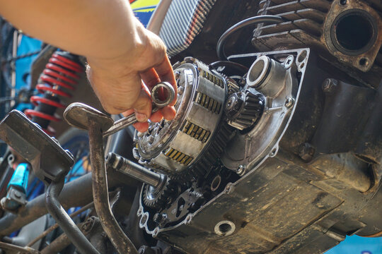The process of manually repairing or servicing a motorcycle engine by a mechanic. The mechanic's hands are seen removing or installing a cover component near the cylinder block of a two-stroke engine.