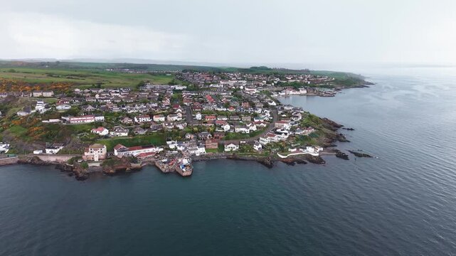 Aerial cinematic forward flyover of Pettycur coastal village houses and scenic rocky shoreline, Fife, Scotland